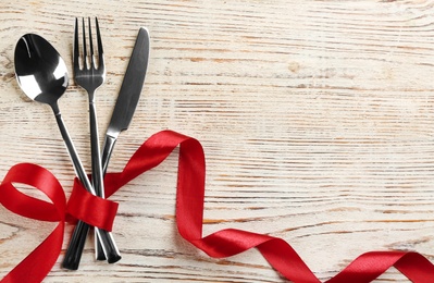Photo of Cutlery set and red ribbon on white wooden  background, flat lay with space for text. Valentine's Day dinner