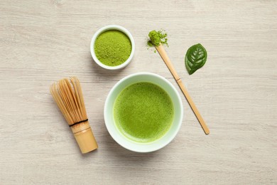 Photo of Cup of fresh matcha tea, bamboo whisk, spoon and green powder on wooden table, flat lay