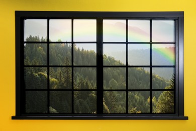 View of beautiful rainbow in mountains through window