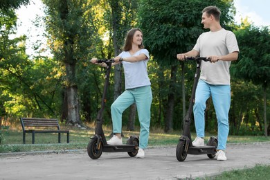 Happy couple riding modern electric kick scooters in park