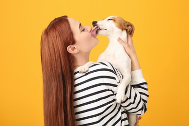 Photo of Woman kissing cute Jack Russell Terrier dog on orange background, back view