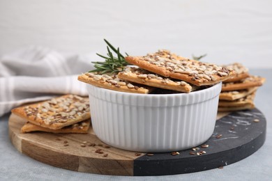 Photo of Cereal crackers with flax, sunflower, sesame seeds and rosemary in bowl on grey table, closeup