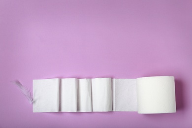 Photo of Roll of toilet paper and feather on color background, top view. Space for text