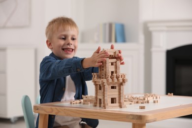 Cute little boy playing with wooden tower at table indoors. Child's toy