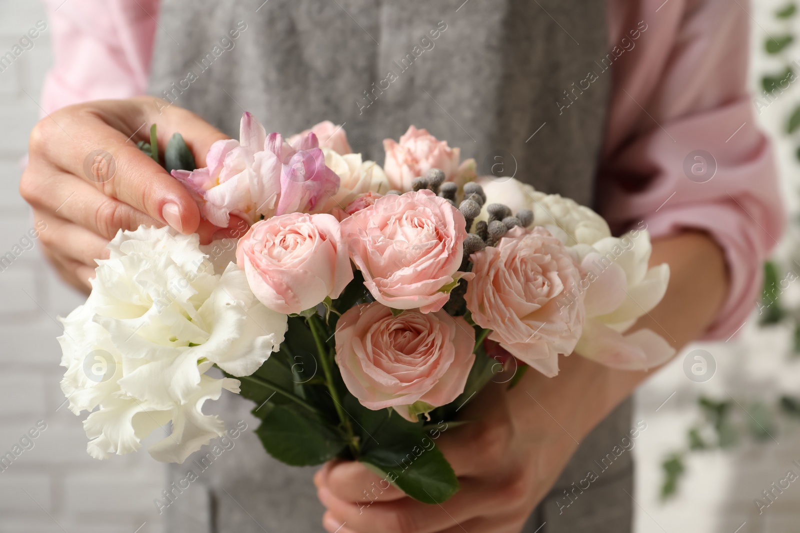 Photo of Florist creating beautiful bouquet with roses indoors, closeup