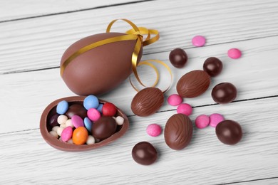 Photo of Delicious chocolate eggs and candies on white wooden table, flat lay