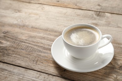 Tasty coffee in cup on wooden table, closeup. Space for text