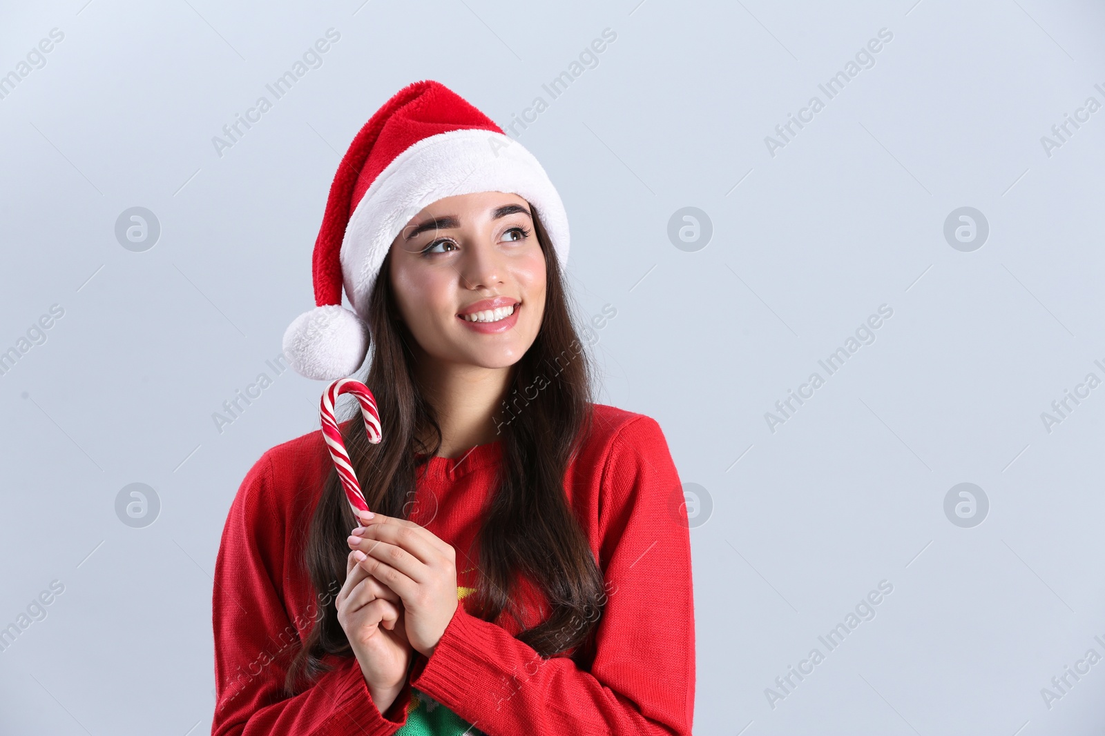 Photo of Beautiful woman in Santa Claus hat holding candy cane on light grey background. Space for text