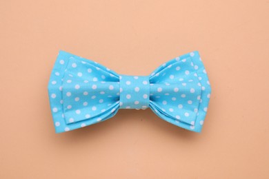 Stylish light blue bow tie with polka dot pattern on pale orange background, top view