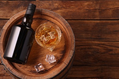 Photo of Whiskey with ice cubes in glass, bottle and barrel on wooden table, top view. Space for text