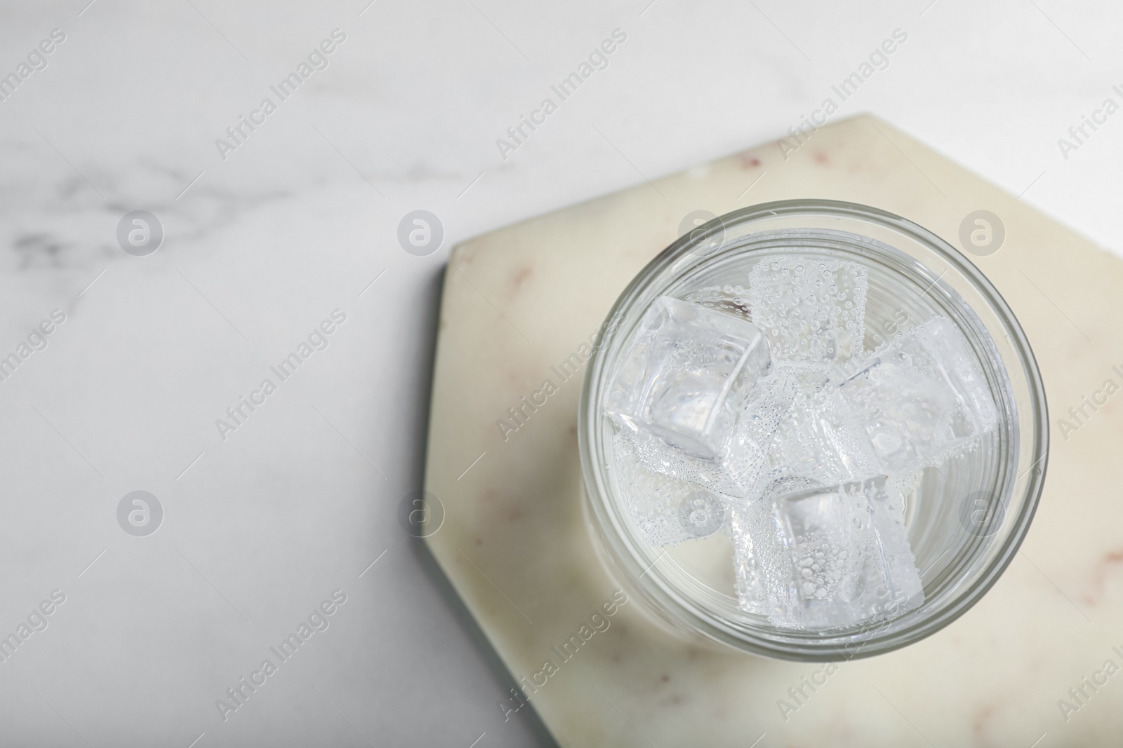 Photo of Glass of soda water with ice on white marble table, top view. Space for text