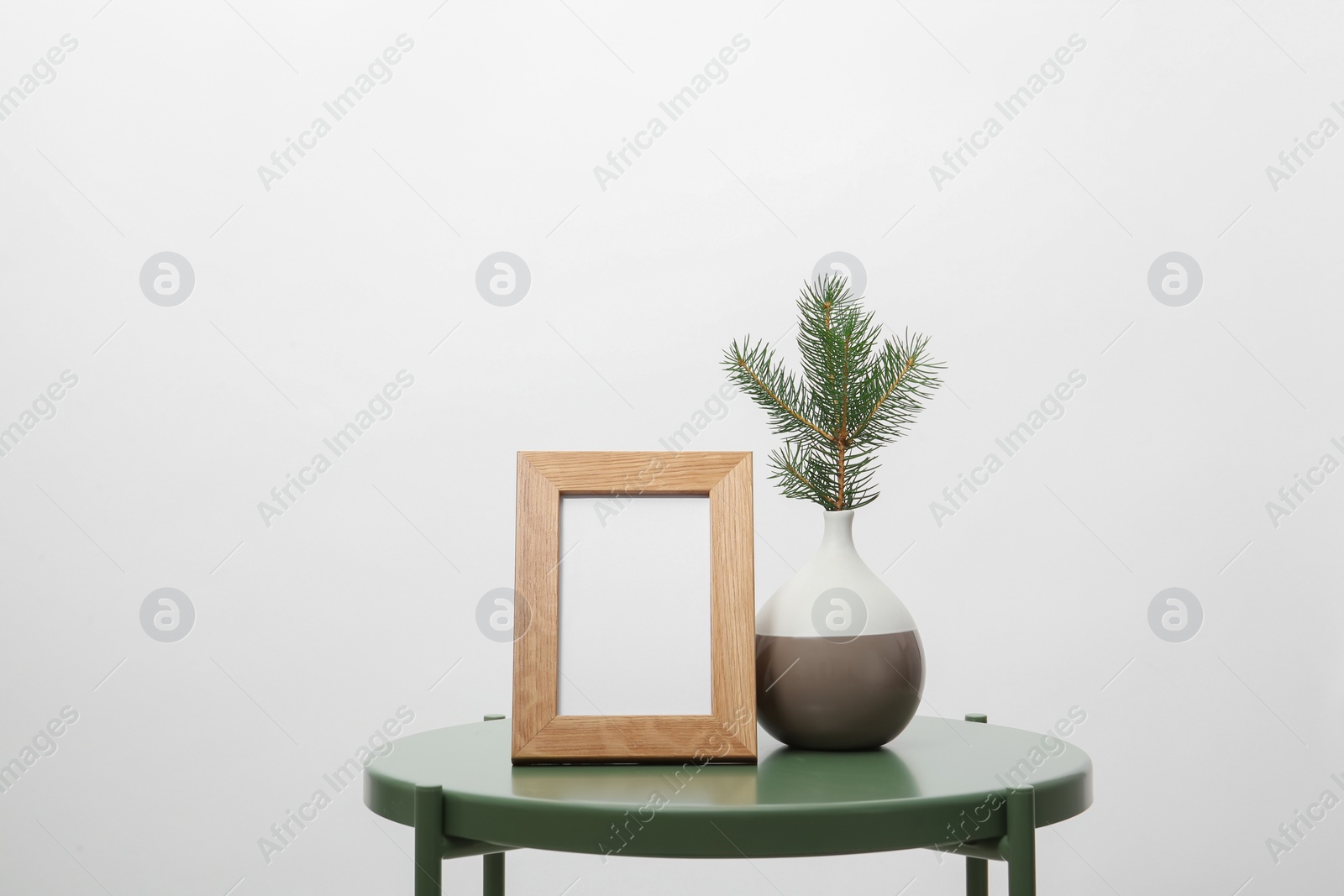 Photo of Blank frame and vase with fir branch on table against white background. Mock up for design