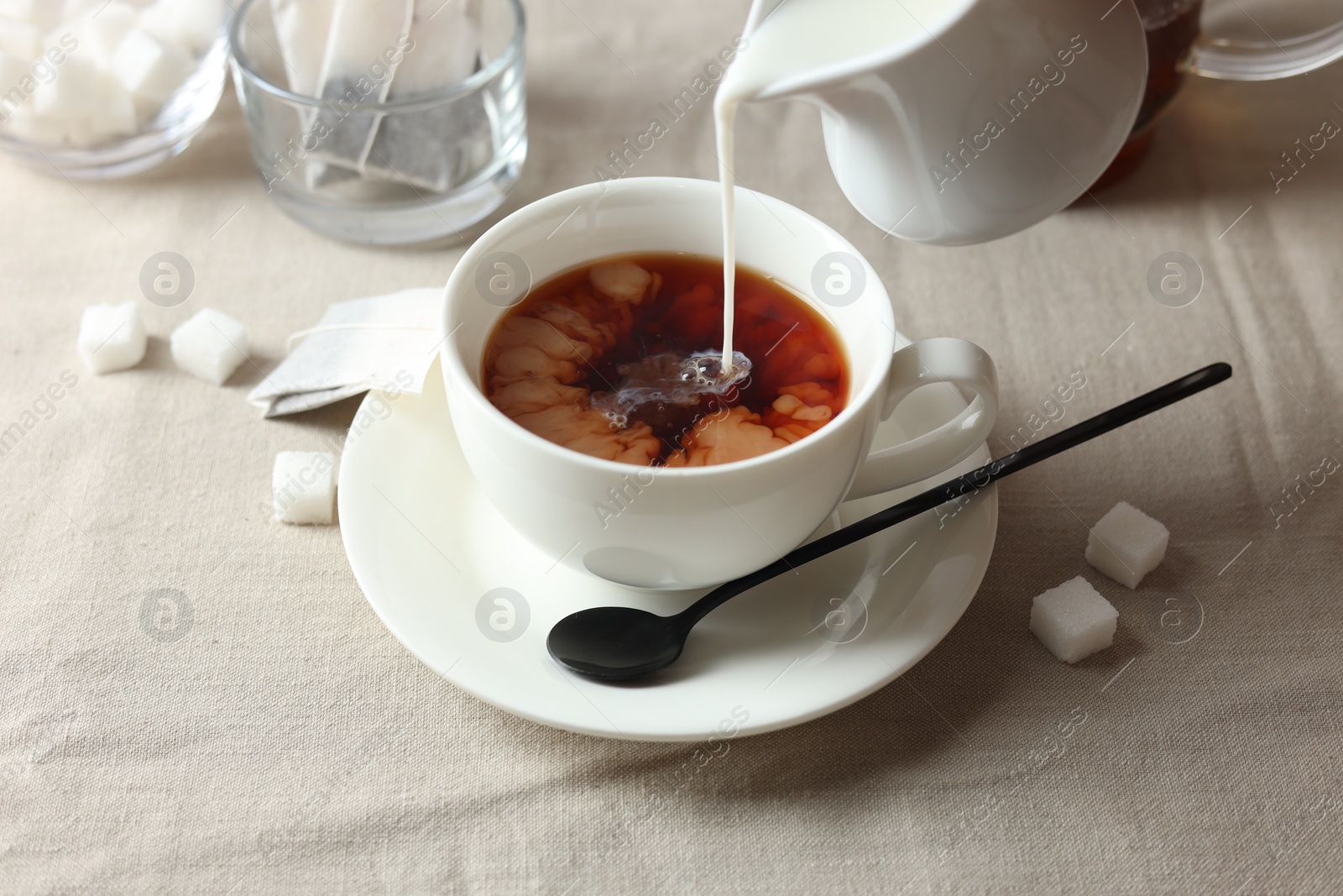 Photo of Pouring milk into cup with tea on light table, closeup