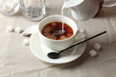 Photo of Pouring milk into cup with tea on light table, closeup