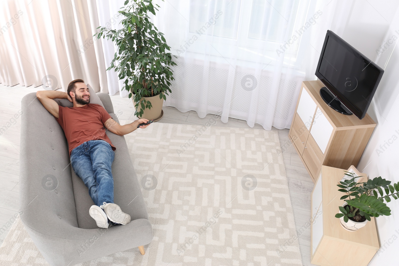 Photo of Handsome young man watching TV on sofa at home