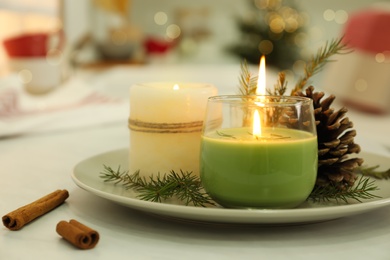 Photo of Burning scented conifer candles and pine cone on white table