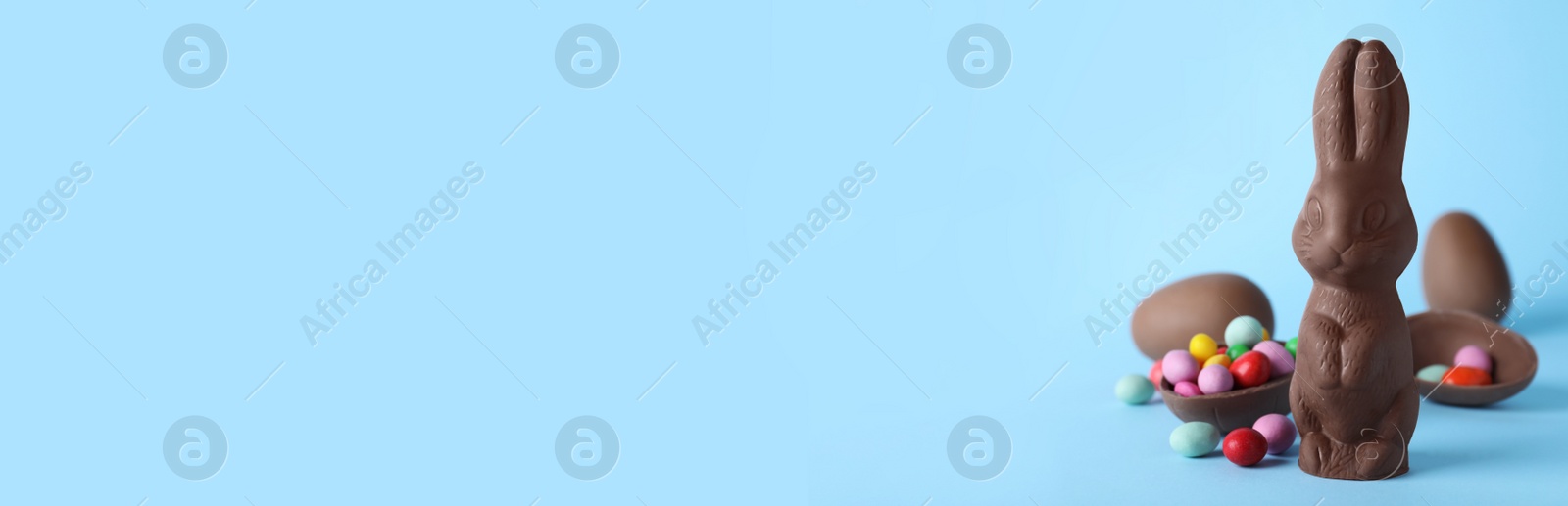 Photo of Chocolate Easter bunny and eggs on light blue background. Space for text