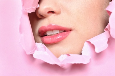 Photo of View of beautiful young woman with perfect lips makeup through hole in color paper