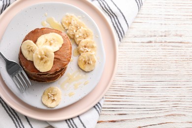 Photo of Plate of banana pancakes with honey served on white wooden table, top view. Space for text
