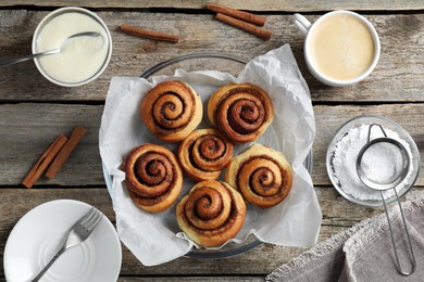 Photo of Tasty cinnamon rolls and ingredients on wooden table, flat lay