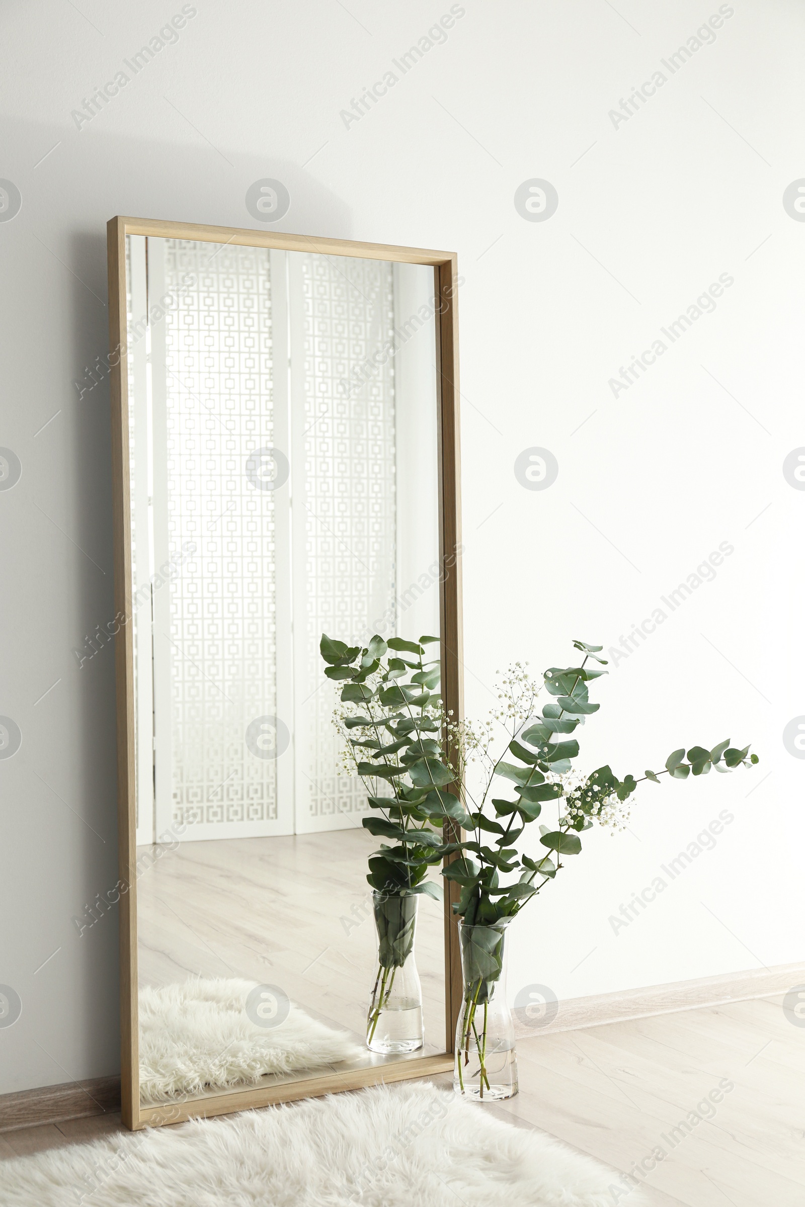 Photo of Large mirror with wooden frame near white wall in light room