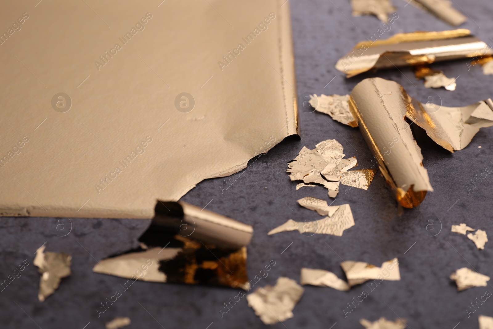 Photo of Edible gold leaf on grey textured table, closeup