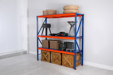 Photo of Metal shelving unit with wooden crates and different household stuff near light wall indoors
