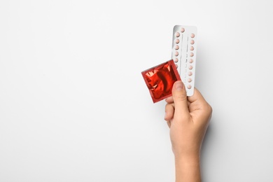 Photo of Woman holding condom and birth control pills on white background, top view. Safe sex