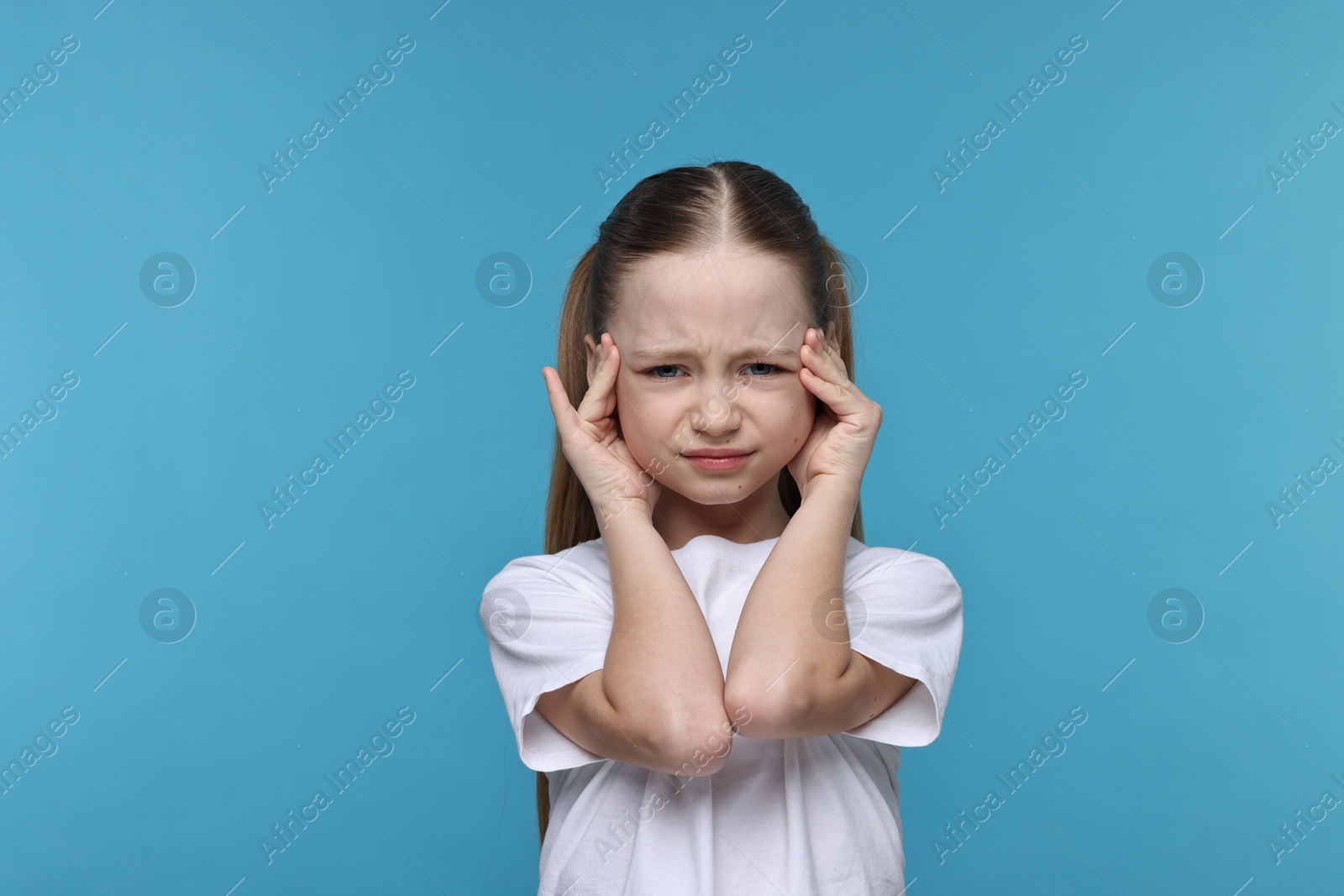 Photo of Little girl suffering from headache on light blue background
