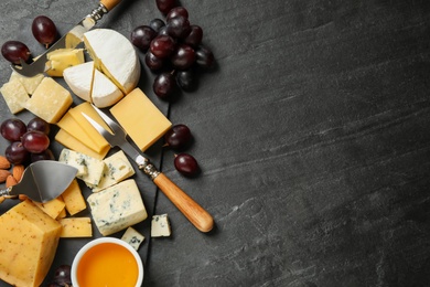 Photo of Cheese platter with specialized knives and fork on dark table, top view. Space for text