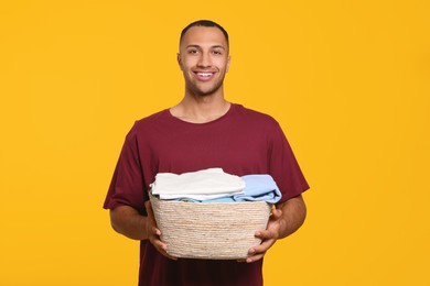 Happy man with basket full of laundry on orange background