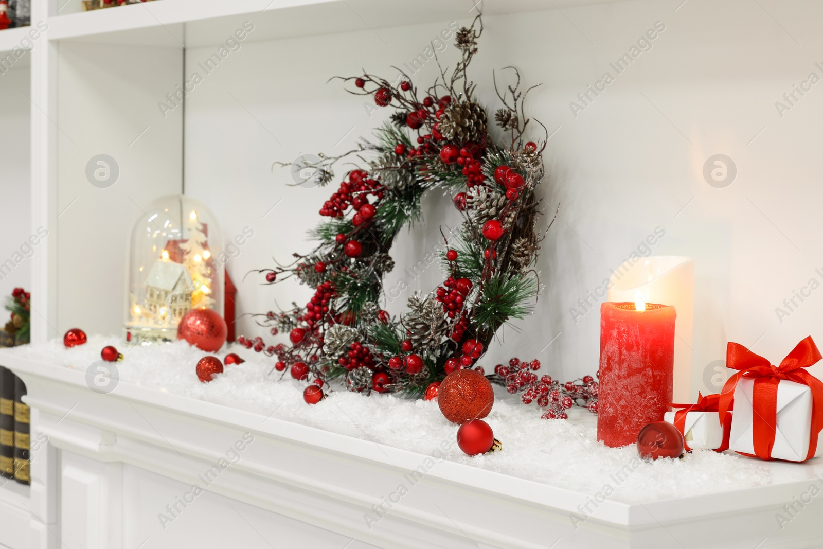 Photo of Beautiful Christmas decoration with artificial snow and burning candles on fireplace indoors