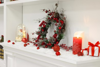 Beautiful Christmas decoration with artificial snow and burning candles on fireplace indoors