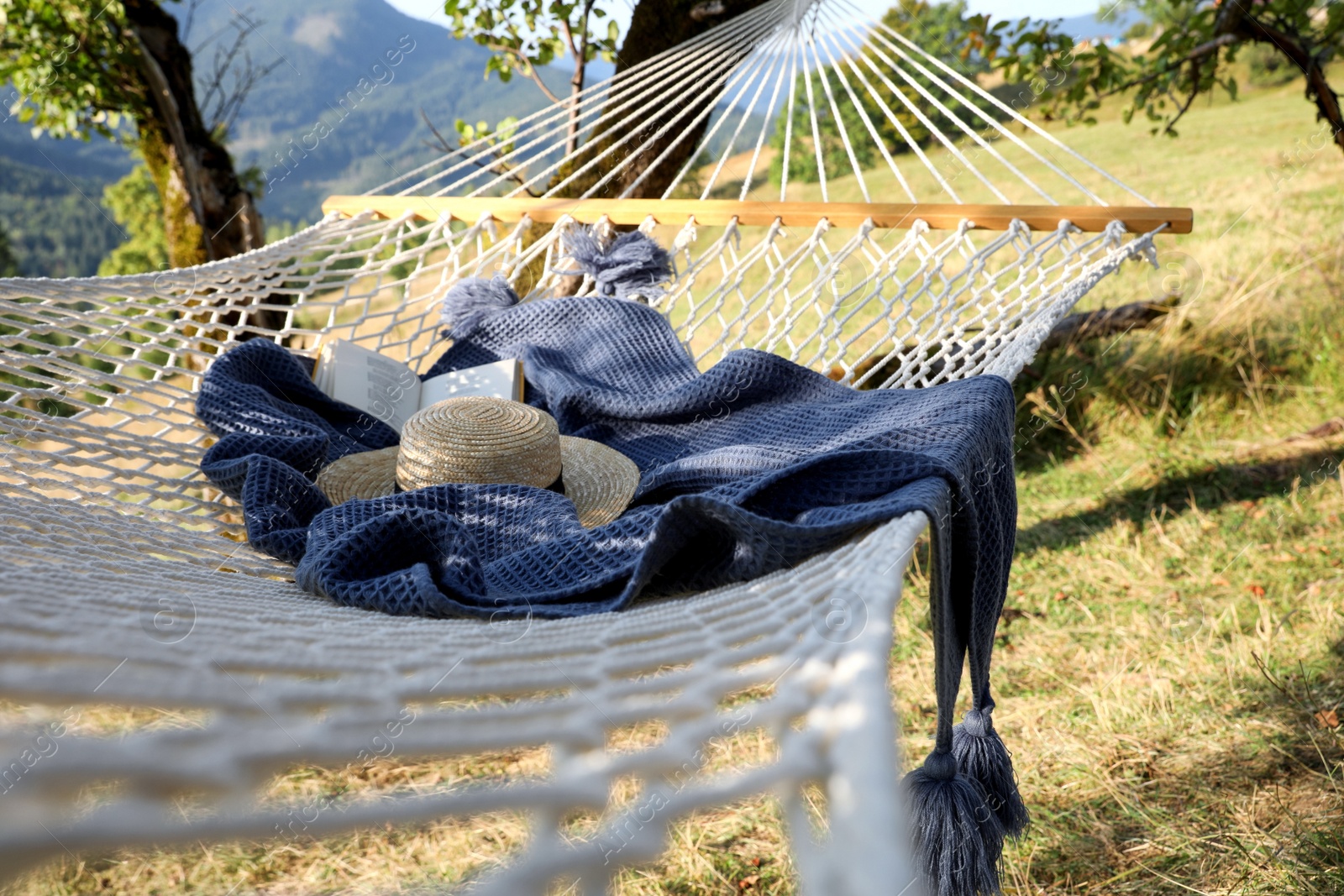 Photo of Comfortable net hammock with hat, book and blanket in mountains on sunny day