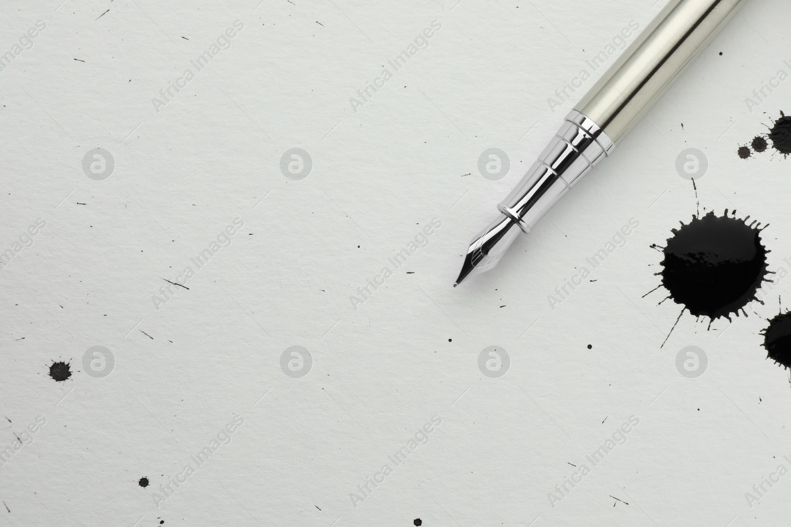 Photo of Stylish fountain pen on paper with drops of ink, top view. Space for text