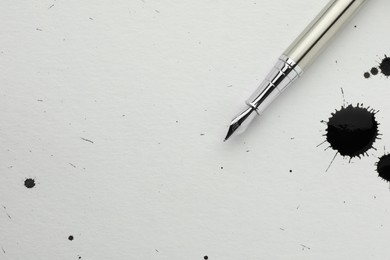 Stylish fountain pen on paper with drops of ink, top view. Space for text