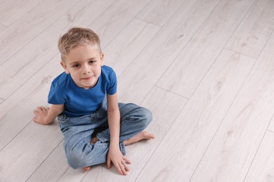 Photo of Cute little boy sitting on warm floor indoors, space for text. Heating system