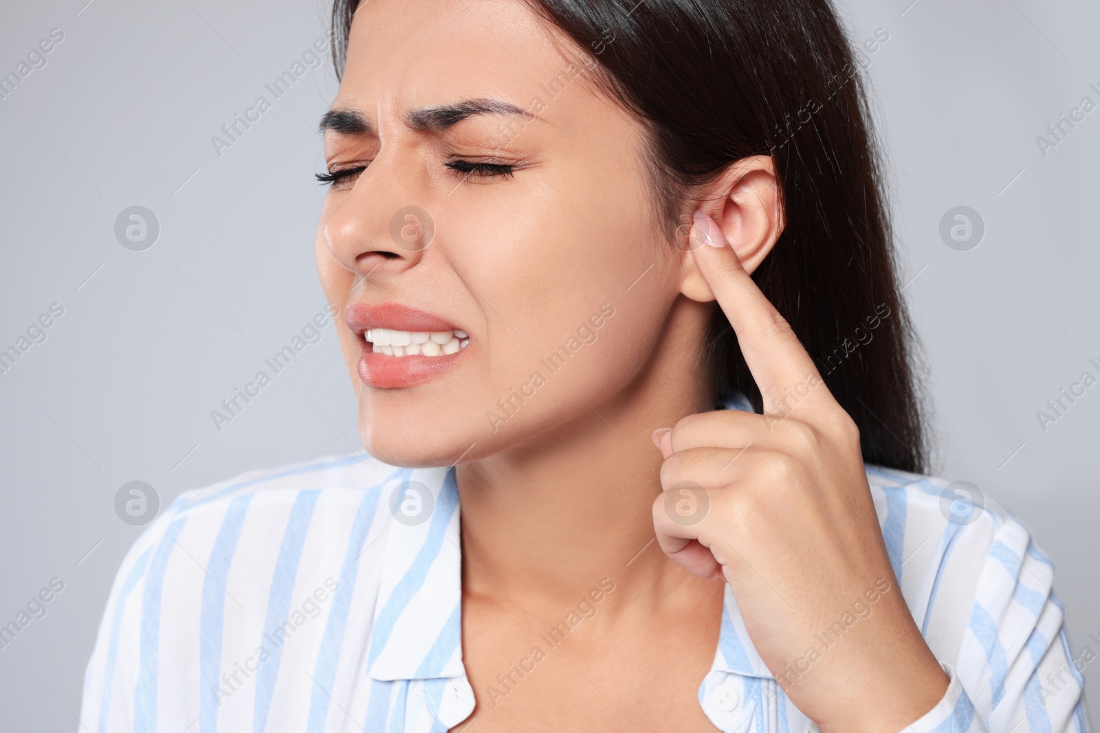 Photo of Emotional young woman suffering from ear pain on light grey background, closeup