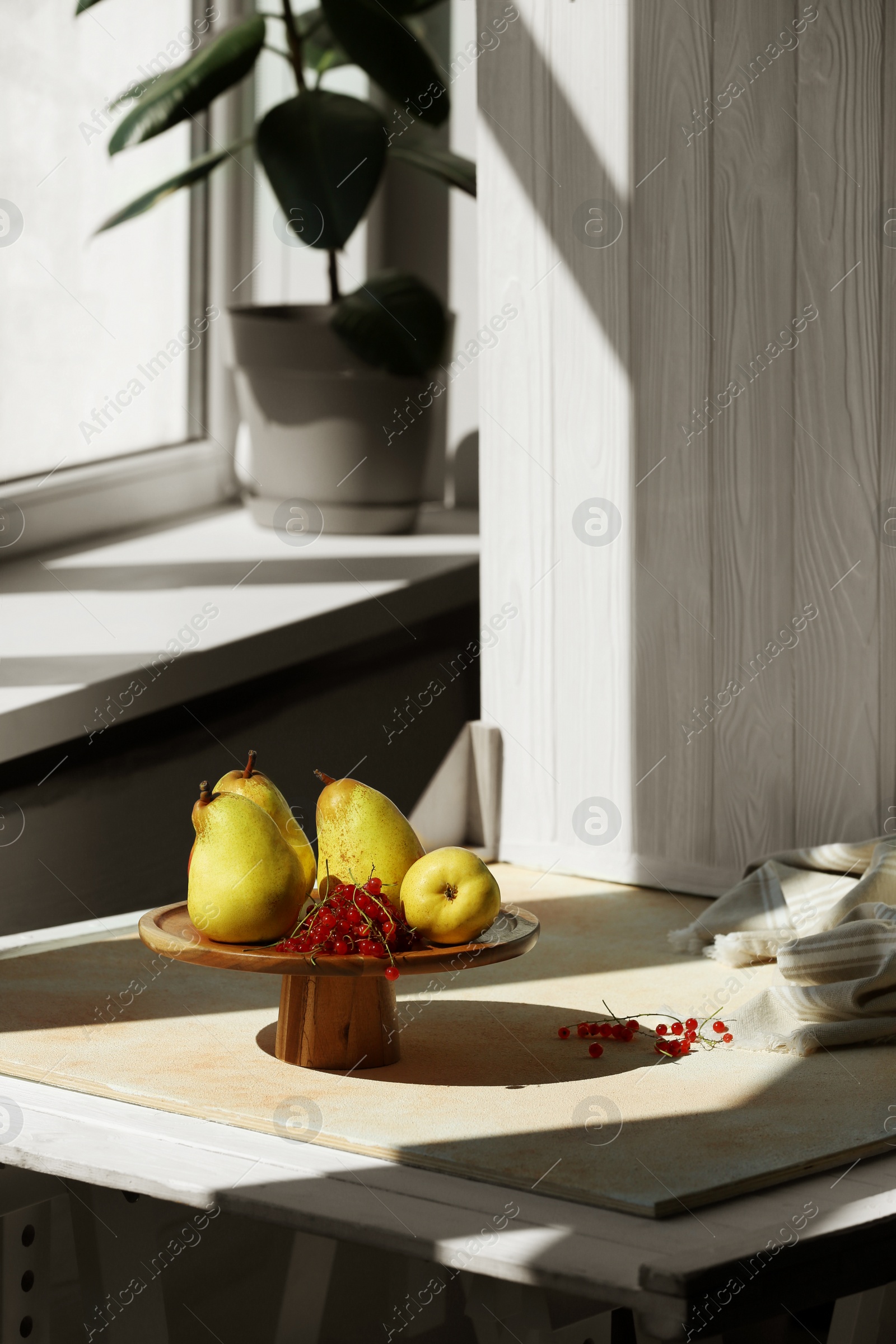 Photo of Stand with juicy pears, red currants and double-sided backdrop on table in photo studio