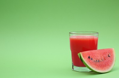 Photo of Glass of delicious drink and cut fresh watermelon on light green background, space for text