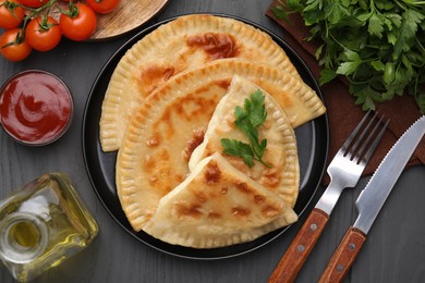 Delicious fried chebureki with cheese, parsley and ingredients served on grey wooden table, flat lay