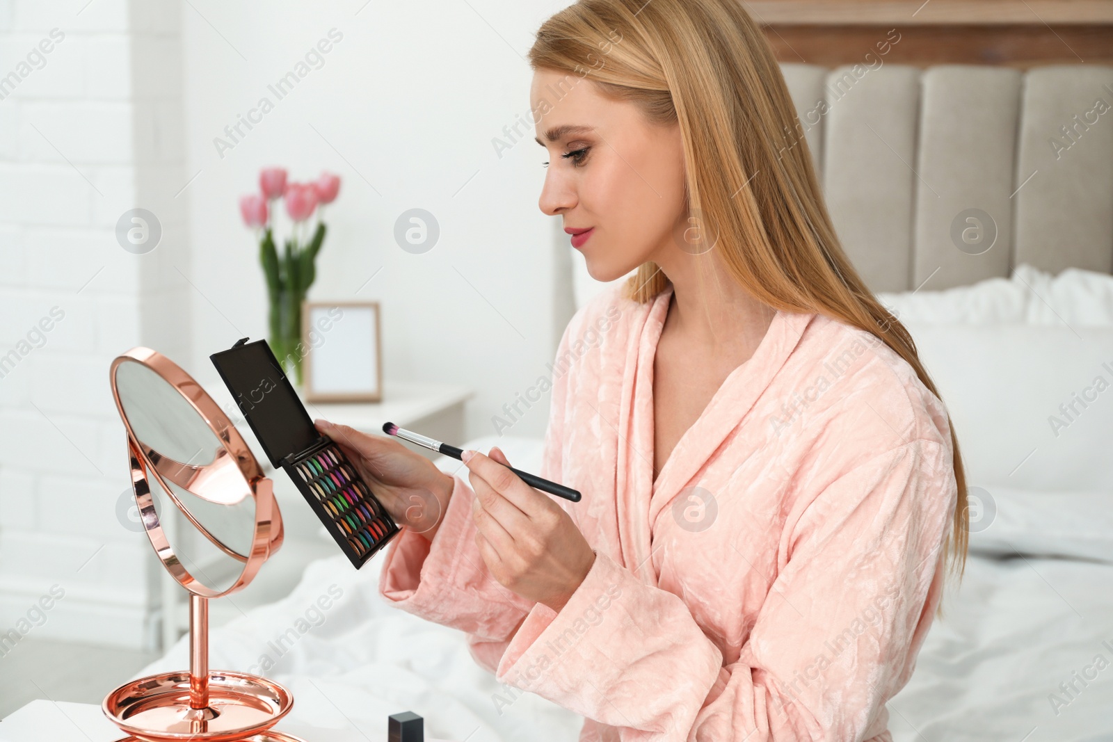 Photo of Beautiful woman with mirror applying makeup in bedroom