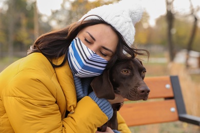 Photo of Woman in protective mask with German Shorthaired Pointer outdoors. Walking dog during COVID-19 pandemic