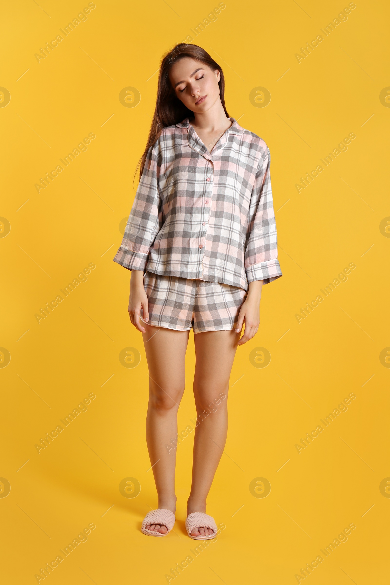 Photo of Young woman wearing pajamas and slippers in sleepwalking state on yellow background