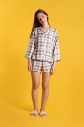 Photo of Young woman wearing pajamas and slippers in sleepwalking state on yellow background
