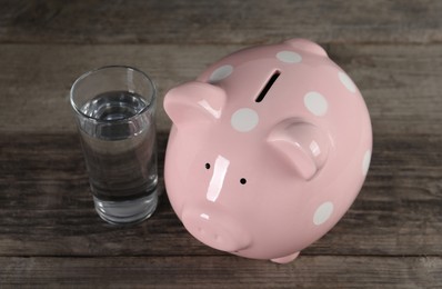 Photo of Water scarcity concept. Piggy bank and glass of drink on wooden table