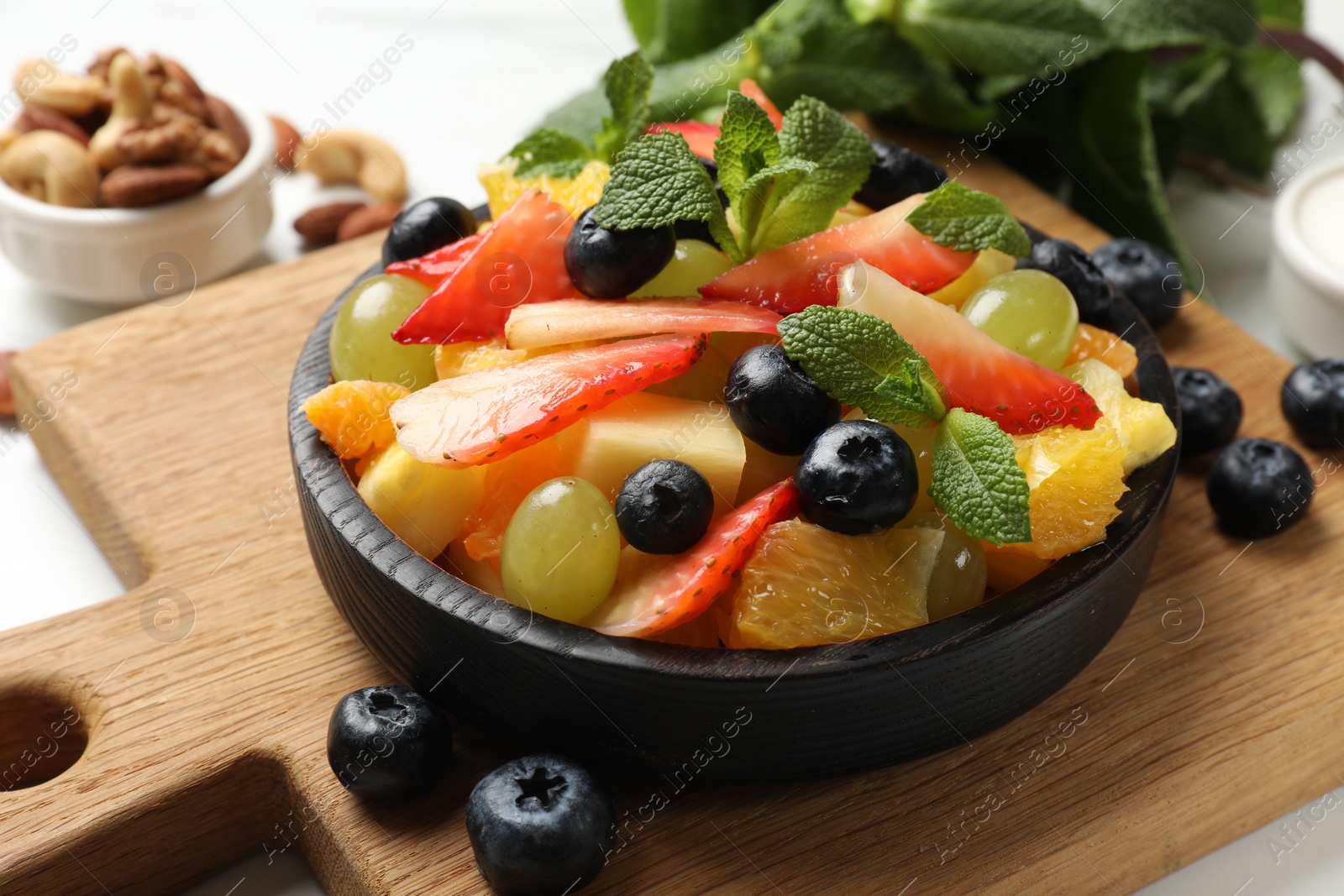 Photo of Delicious fruit salad in bowl, berries, nuts and fresh mint on white table