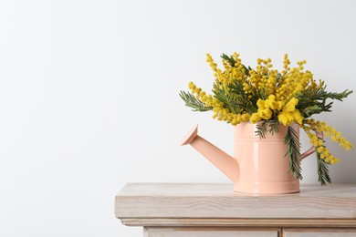 Beautiful mimosa flowers in watering can on wooden table, space for text
