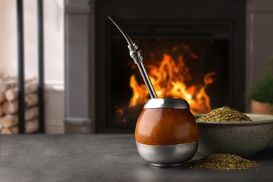 Image of Calabash with mate tea and bombilla on light grey table near fireplace. Space for text