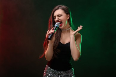 Emotional woman with microphone singing in color lights on dark background